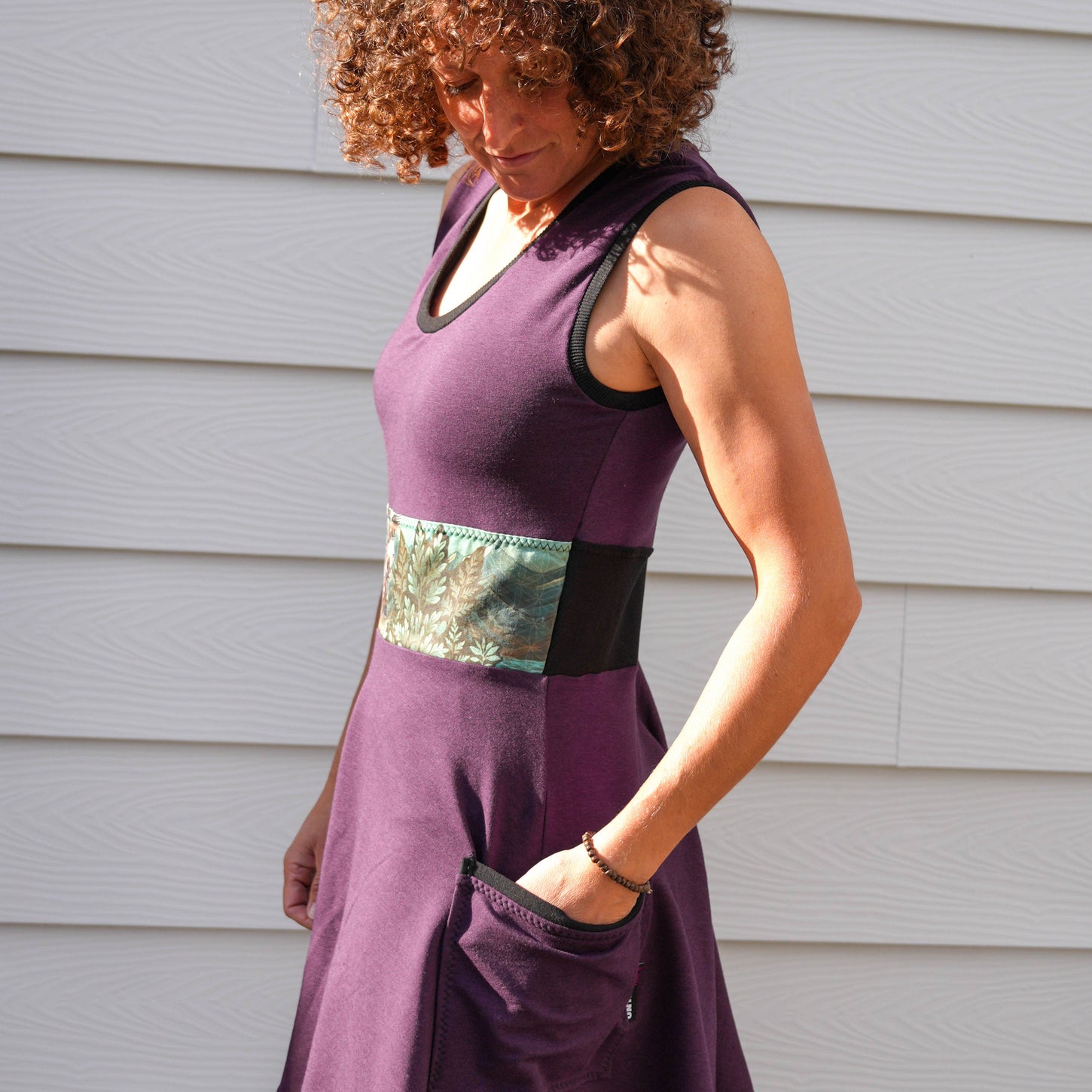 Woman wearing a purple dress with a belt standing against a gray wall.