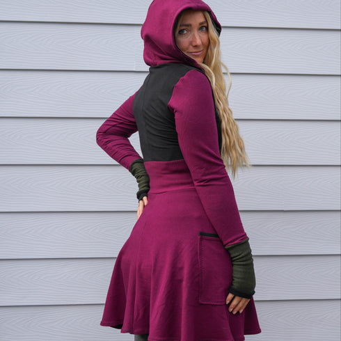 Woman wearing a purple and black hoodie dress standing against a gray wall.