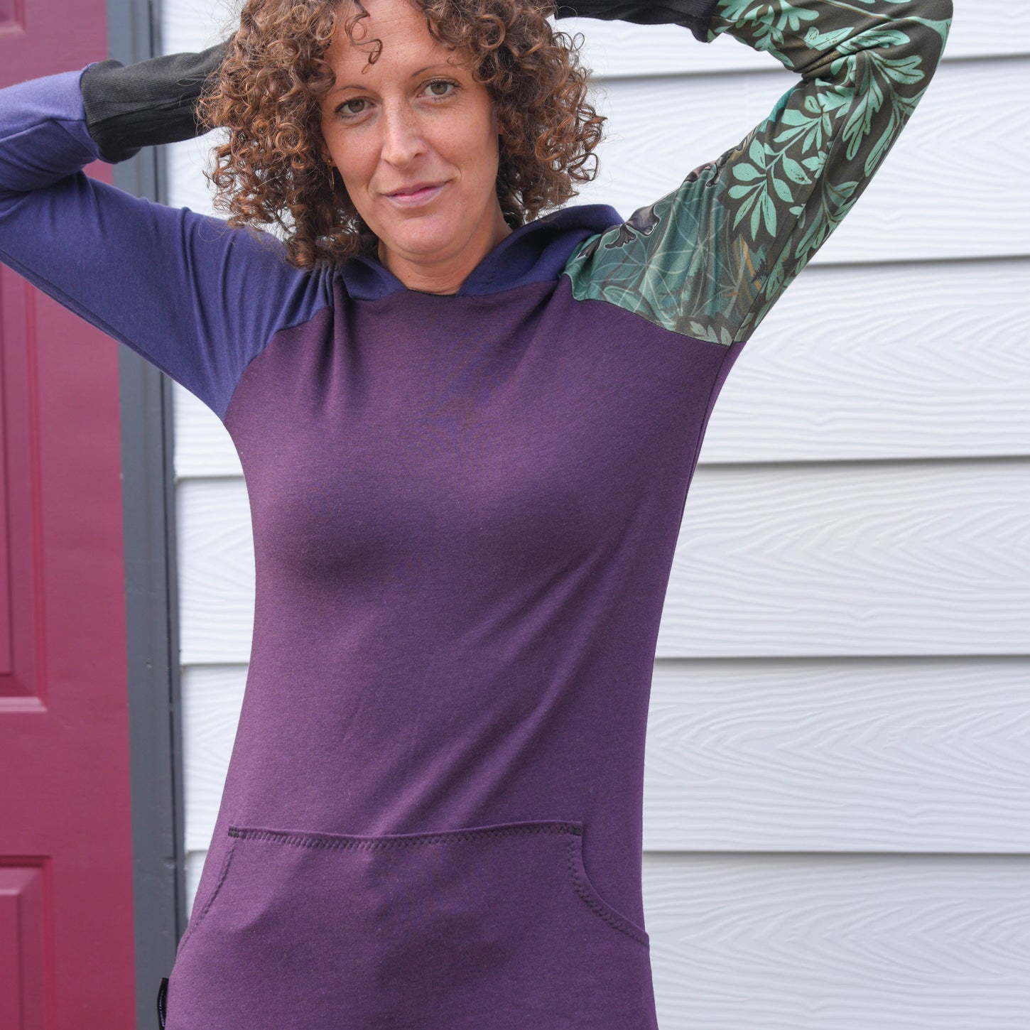 Person wearing a purple hoodie with green sleeves in front of a white wall.