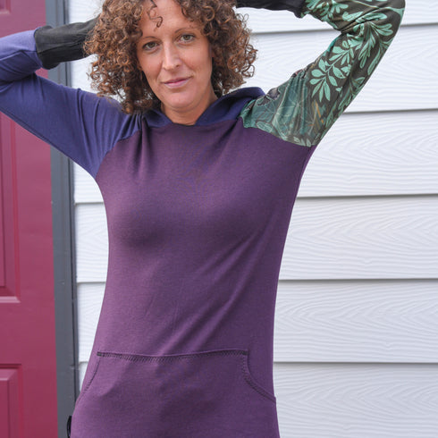 Person wearing a purple hoodie with green sleeves in front of a white wall.