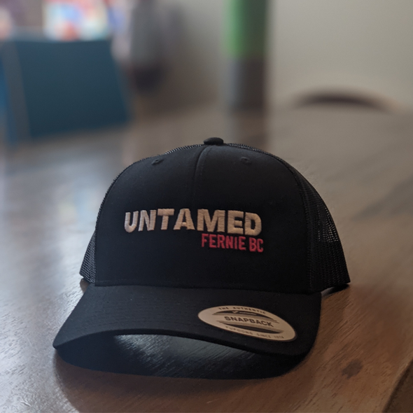 Black Flex fit baseball cap with pink embroidery slogan saying Untamed Fernie, BC 